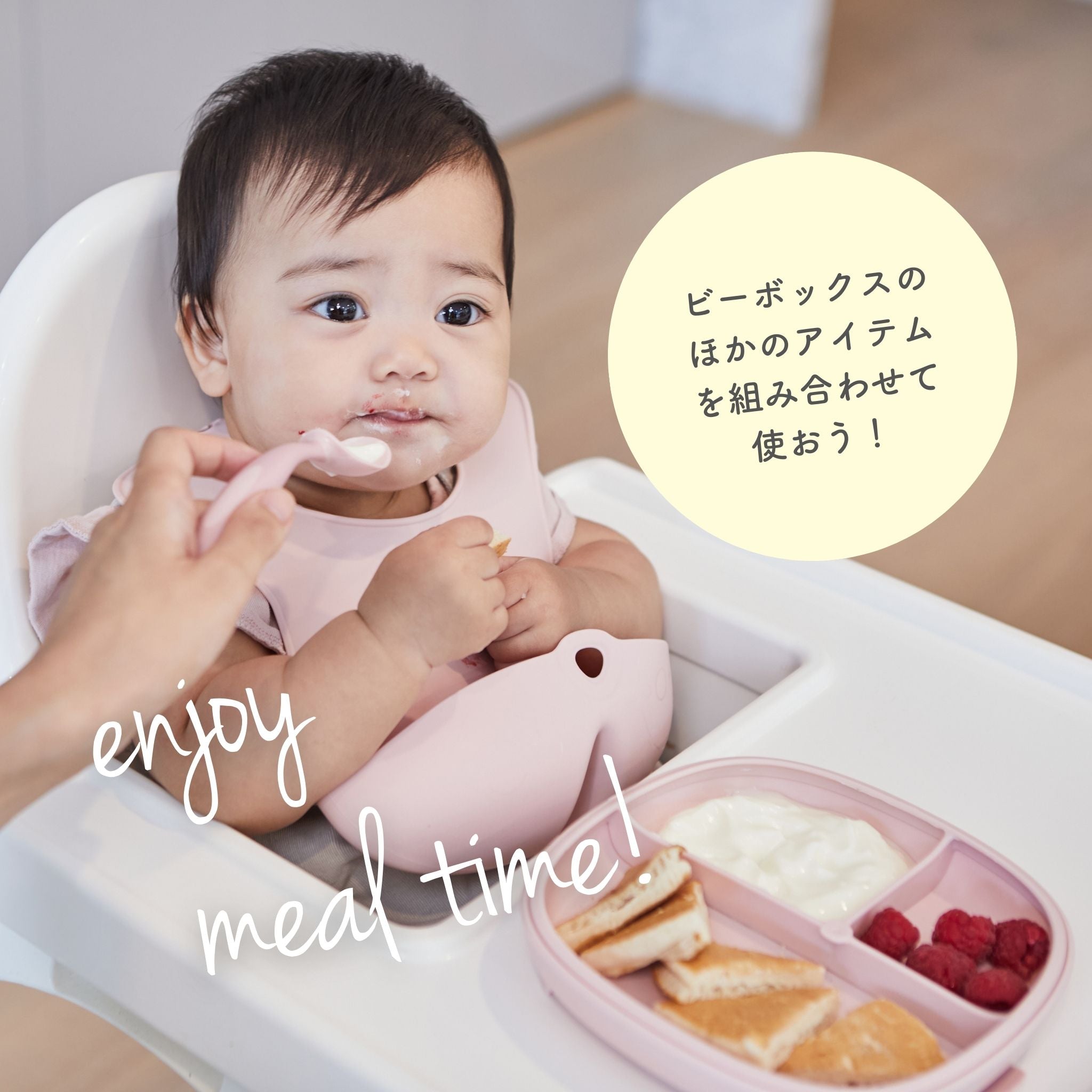 ピンクのスタイを着けた赤ちゃんがハイチェアに座り、スプーンで食事をしている。トレーにはパン、ヨーグルト、ラズベリーがあり、左下に「enjoy meal time!」、右側に「ビーボックスのほかのアイテムを組み合わせて使おう！」のテキストがある。