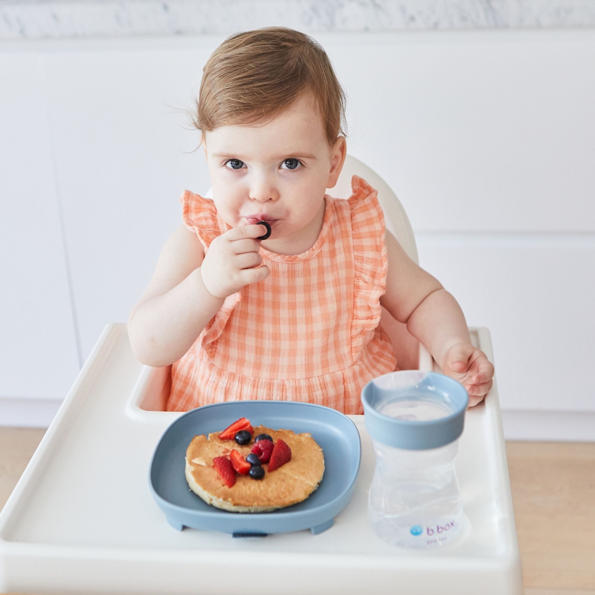 ハイチェアに座った女の子が幼児プレートに盛り付けられたホットケーキを食べている様子
