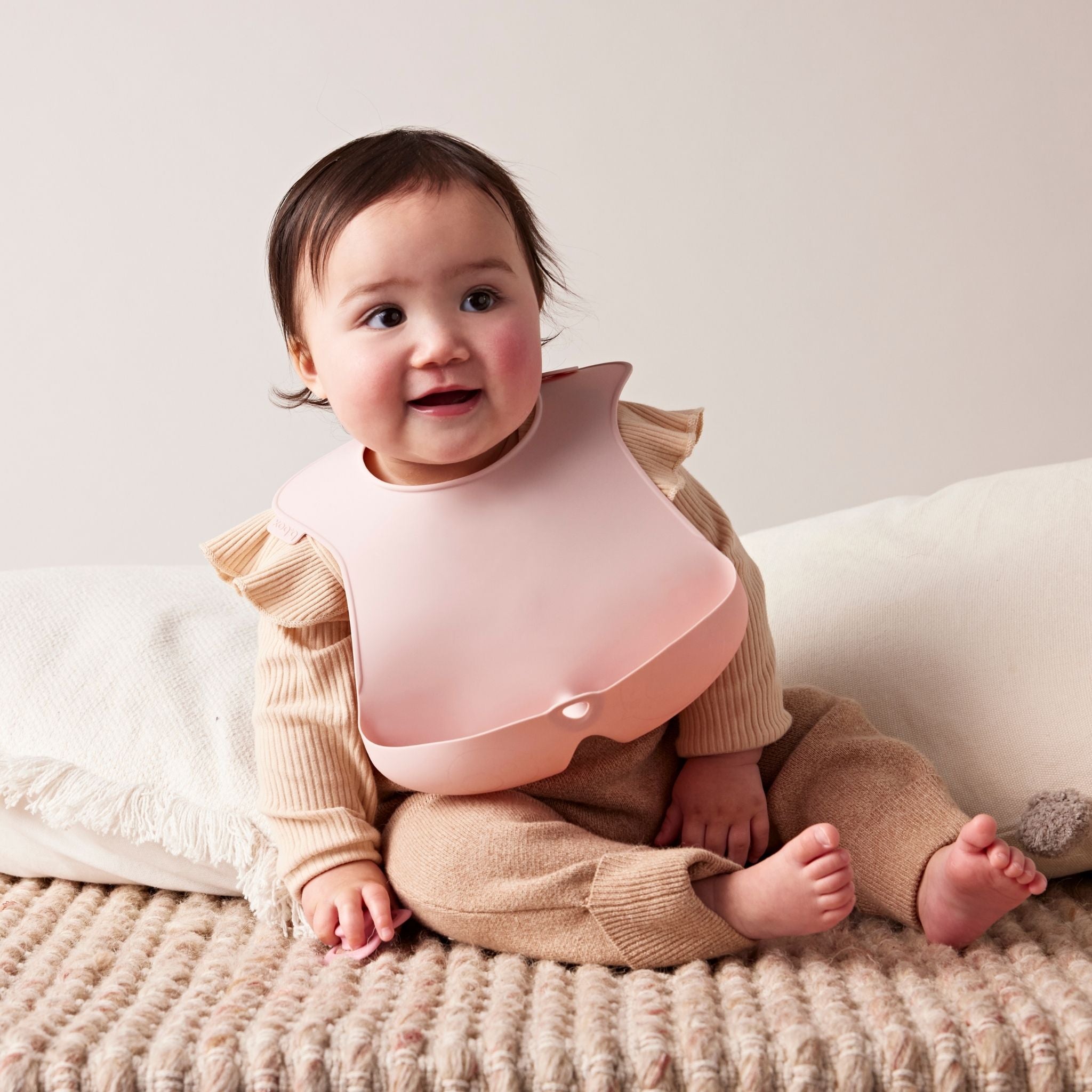 ビーボックスのシリコンビブをつけている女の子の赤ちゃんが笑顔で座っている